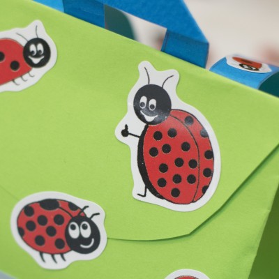Ein Close-uü einer grünen Geschenktüte in Schulranzenform. Diese wurde mit Marienkäfer-Stickern von Avery Zweckform beklebt.