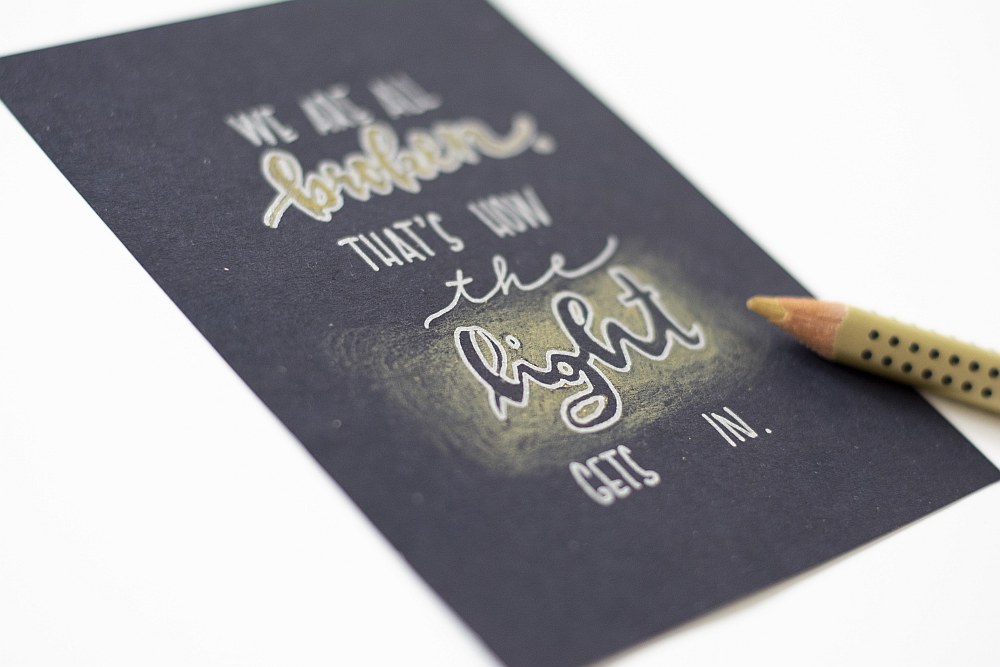 Handlettering „We are all broken, that’s how the light gets in“ auf schwarzer Karte.
