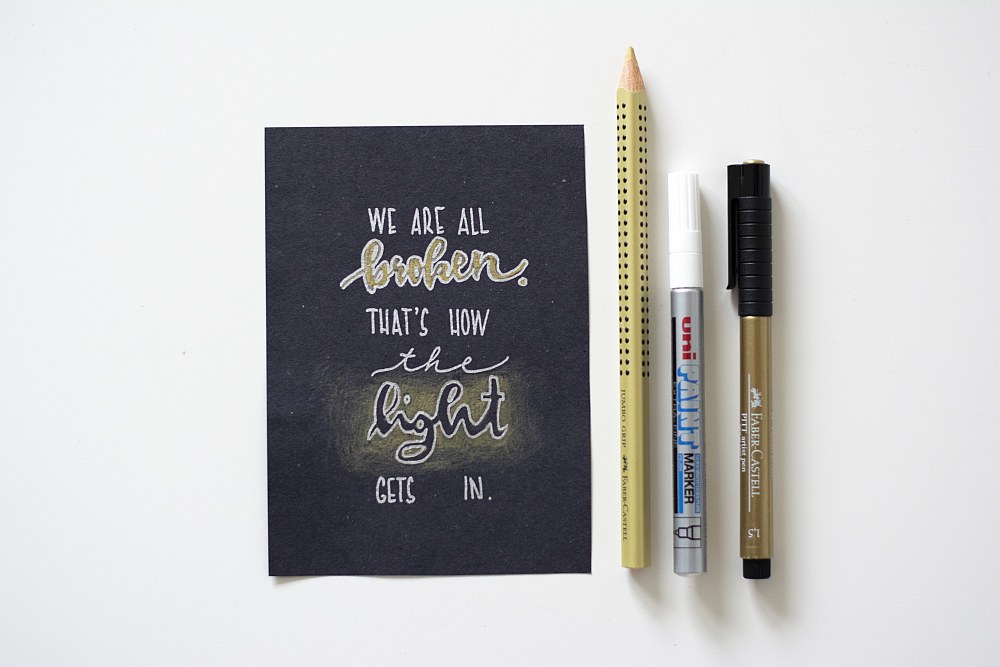 Schwarze Karte mit Lettering „We are all broken…“ und drei verschiedenen Stiften.