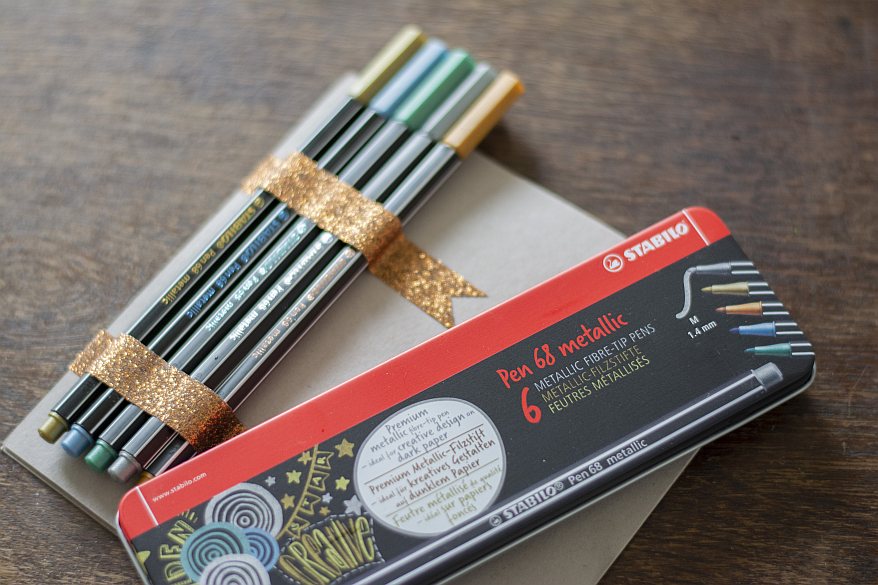 Metallic-Stifte von STABILO mit Glitzerband auf einer Karte befestigt, daneben Stiftebox