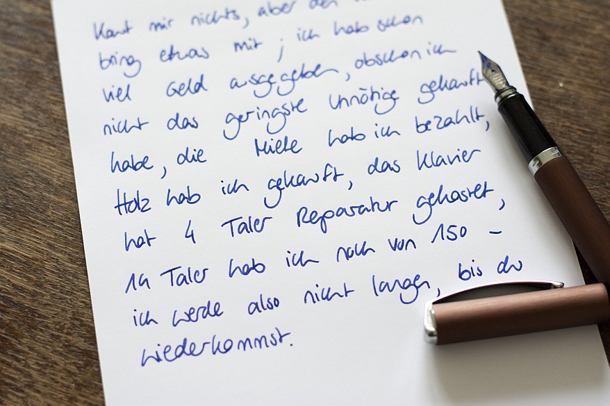 Handgeschriebener Brief in blauer Tinte mit braunem Füllfederhalter der Marke Online daneben.