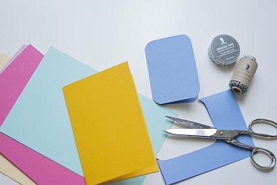 Pastellfarbener Motivkarton von Rössler wird mit Hilfe einer Schere in ein Rechteck mit abgerundeten Ecken zugeschnitten.