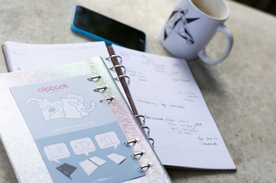 Geöffneter Planer mit handschriftlichen Notizen, Handy und Kaffeetasse daneben.