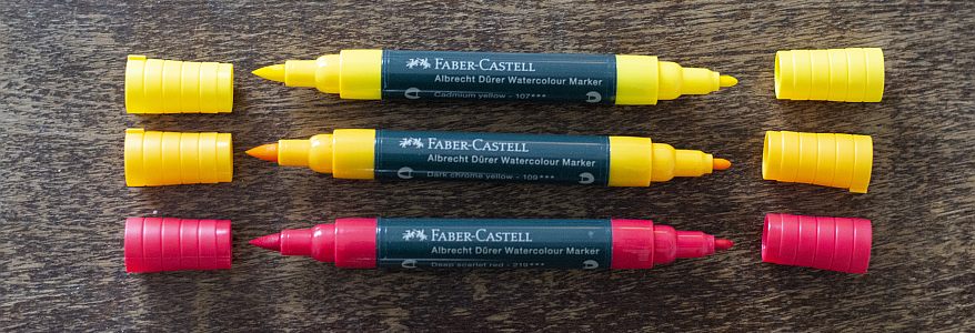 Gelbe und rote Aquarellmarker mit zwei Stiftspitzen liegen auf einem Tisch