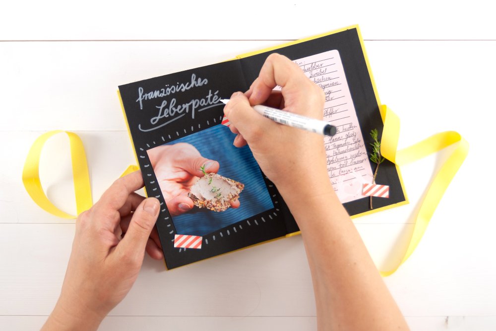 Hand schreibt Notizen in ein gelbes Leporello-Fotoalbum.