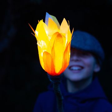 Ein Kind schaut lachend auf eine LED Fackel aus PET-Flaschen, die hell leuchtet.