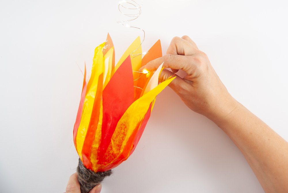 In eine gebastelte Fackel aus PET-Flaschen steckt eine Hand eine Lichterkette.