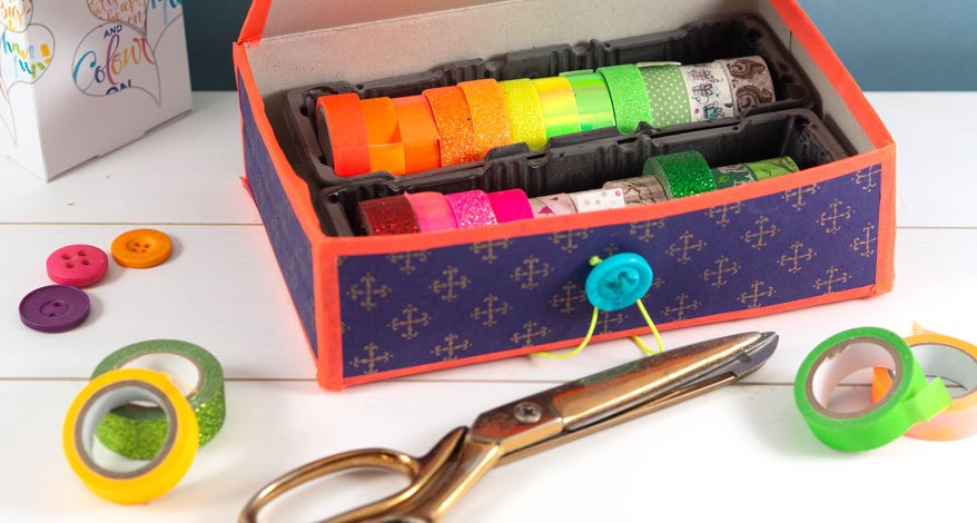 Washi-Tape in bunter DIY-Schachtel mit Schere und Knöpfen auf weißem Tisch