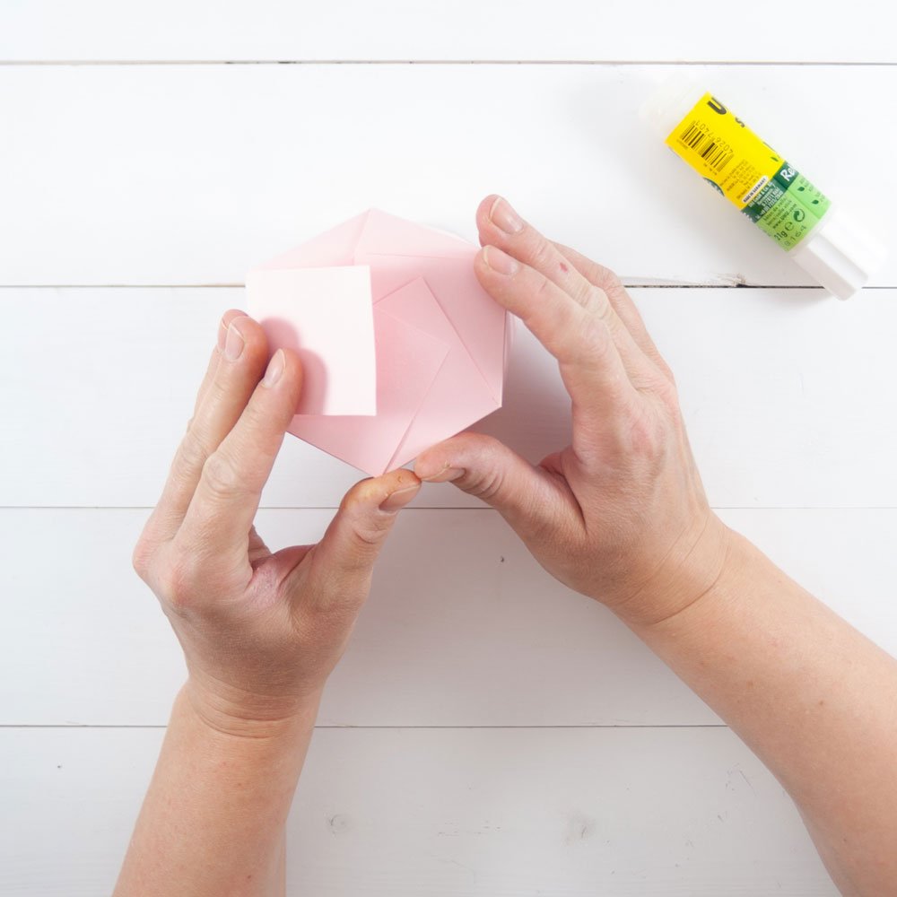 Zwei Hände setzen eine selbstgebastelte Geschenkverpackung zusammen und verkleben sie.