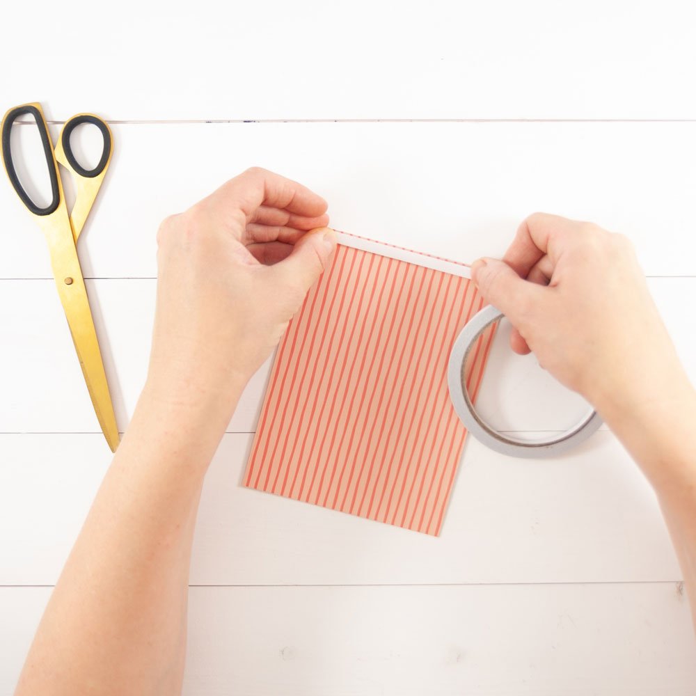 Zwei Händle bringen einen Klebestreifen auf einem Stück Papier auf. Daneben liegt eien Schere.