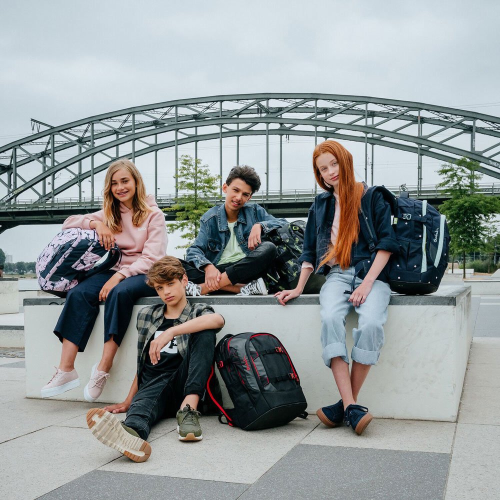 Vier Jugendliche sitzen draußen und schauen in die Kamera. Jeder hat einen Schulrucksack der Marke satch in unterschiedlichen Design dabei.