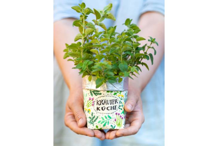 Zwei Hände halten einen selbst bemalten Kräutertopf in die Kamera