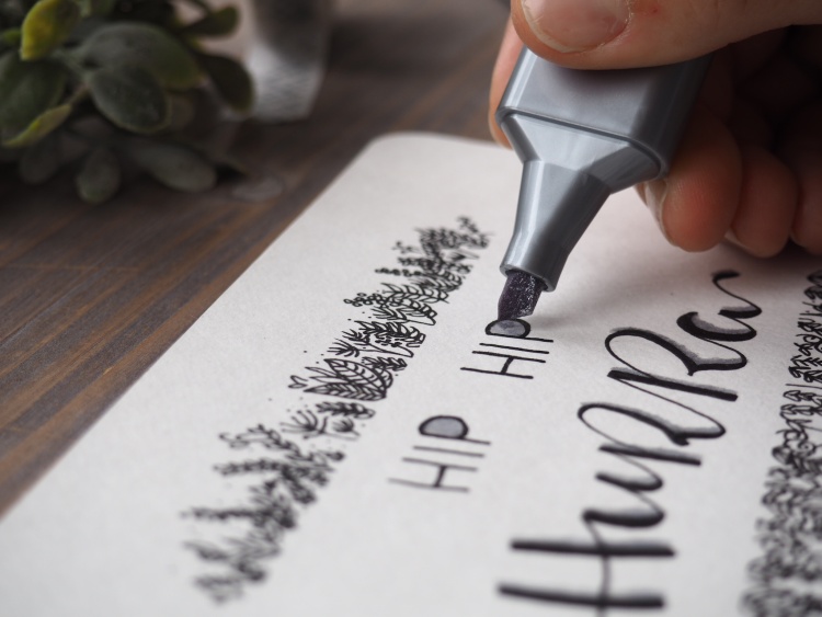 Mit einem silbernen Marker von Faber-Castell wird ein Schriftzug auf einer Karte verziert.
