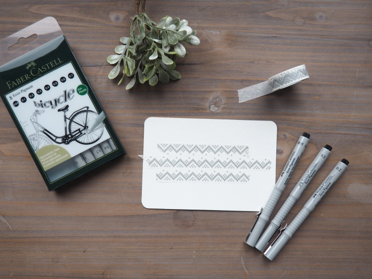 Ein Faber-Castell Set Stifte Set, Washi-Tape und Karte mit Zickzack-Muster liegen auf einem Holzuntergrund.