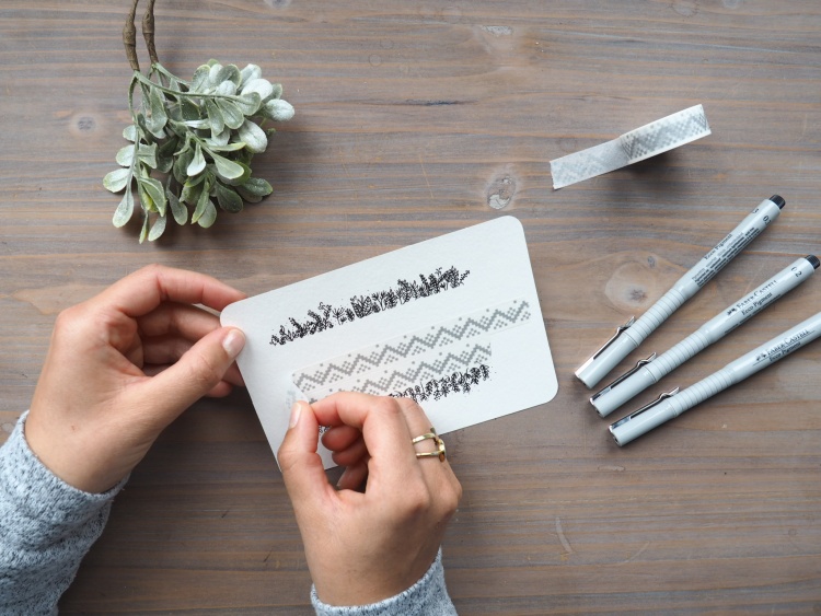 Eine Hand entfernt Washi-Tape von gestalteter Karte.