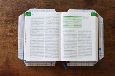 Buch liegt auf Selbstklebefolie zum Einbinden, die Ecken der Folie sind abgeschnitten.