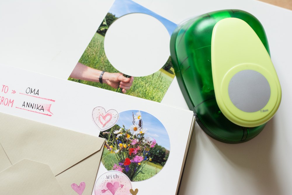 Nahaufnahme eines Stanzegerätes, welches aus einem Foto einen runden Ausschnitt heruasgestanzt hat. Das ausgestanzte Bild ist mit Stickern und anderen Verzierungen in einem Fotoalbum eingeklebt.