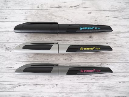 3 Pelikan Füller Active Flow liegen parallel übereinander auf einem grauen Holztisch. 