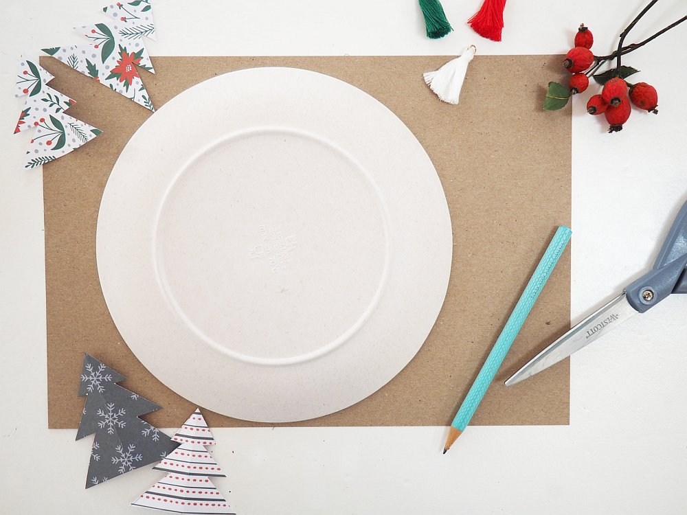 Ein Teller auf einem braunem Karton, Papier, Schere und Dekoelemente daneben.