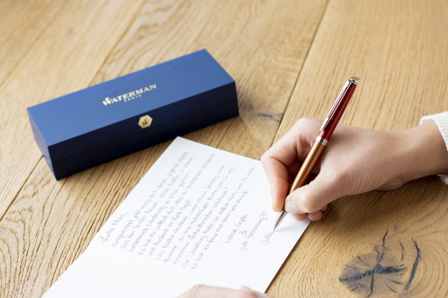 Jemand schreibt eine Karte mit einem Füller. Daneben liegt die Verpackung der Marke Waterman.