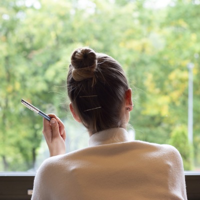 Eine Frau sitzt vor einem Fenser, schaut heraus und hält einen Stift in der Hand.