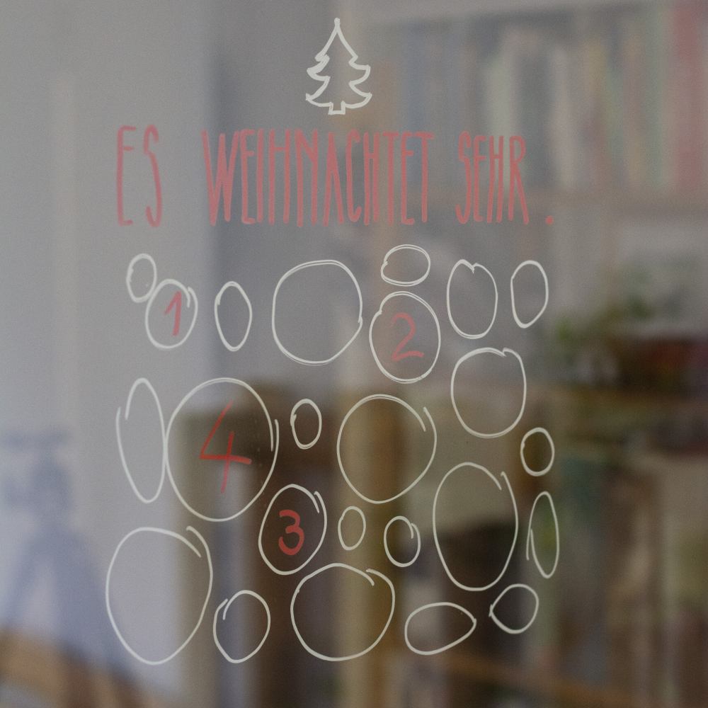 Mehrere Kreise wurden auf ein Fenster gemalt und dienen akls Adventskalender. In drei Kreisen sind Zahlen geschrieben. Über den Kreisen steht "Es weihnachtet sehr" mit einem kleinen Tannenbaum.