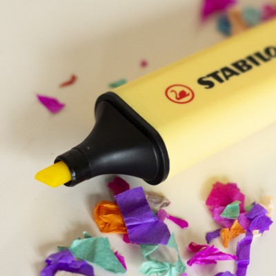 Nahaufnahme eines geöffneten gelben Stabilo Textmarkers neben buntem Konfetti.