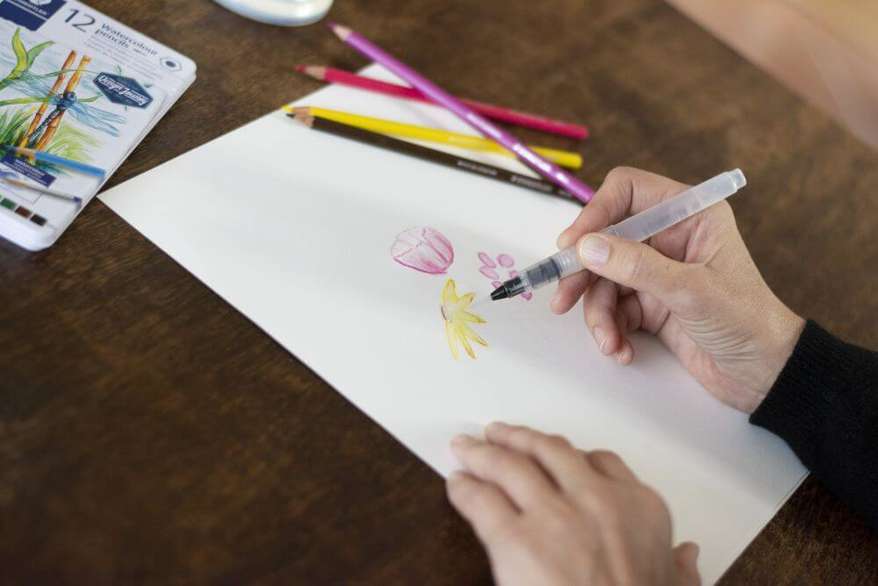 Eine Hand malt mit einem Wassertankpinsel von Staedtler einen Blumenstrauß auf ein Blatt Papier.