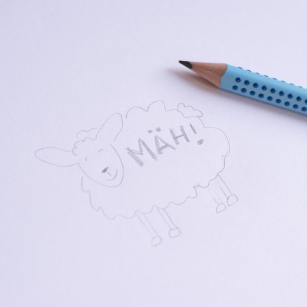 Auf einem Blatt Papier ist ein Schaf gemalt. Daneben ist die Spitze eines Faber-Castell Grip Bleistifts zu sehen.