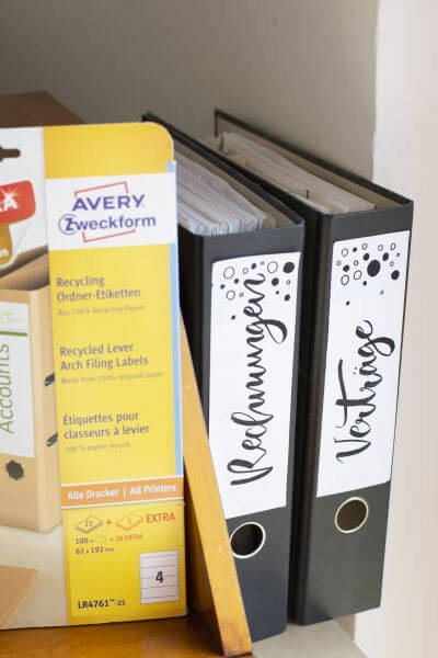 Ordnerrücken von Avery Zweckform mit den Worten "Rechnungen" und "Verträge" in Handlettering.
