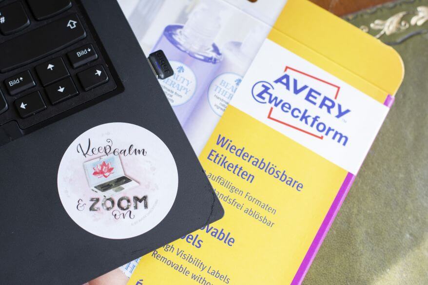 Nahaufnahme eines runden Aufklebers von Avery Zweckform, der auf einem Laptop klebt. Auf ihm steht in Handlettering "Keep calm and zoom on". Im Hintergrund liegt die Verpackung des Aufkleberbogens von Avery Zweckform.