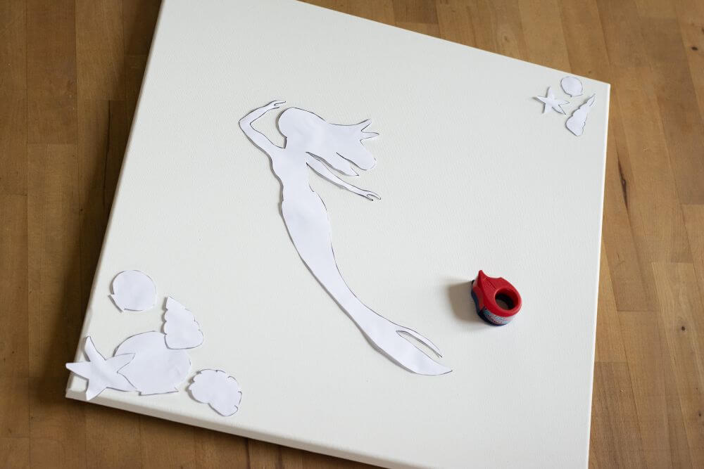 Schablonen aus Papier mit den Formen einer Meerjungfrau und Muscheln werden kleben auf einer Leinwand.