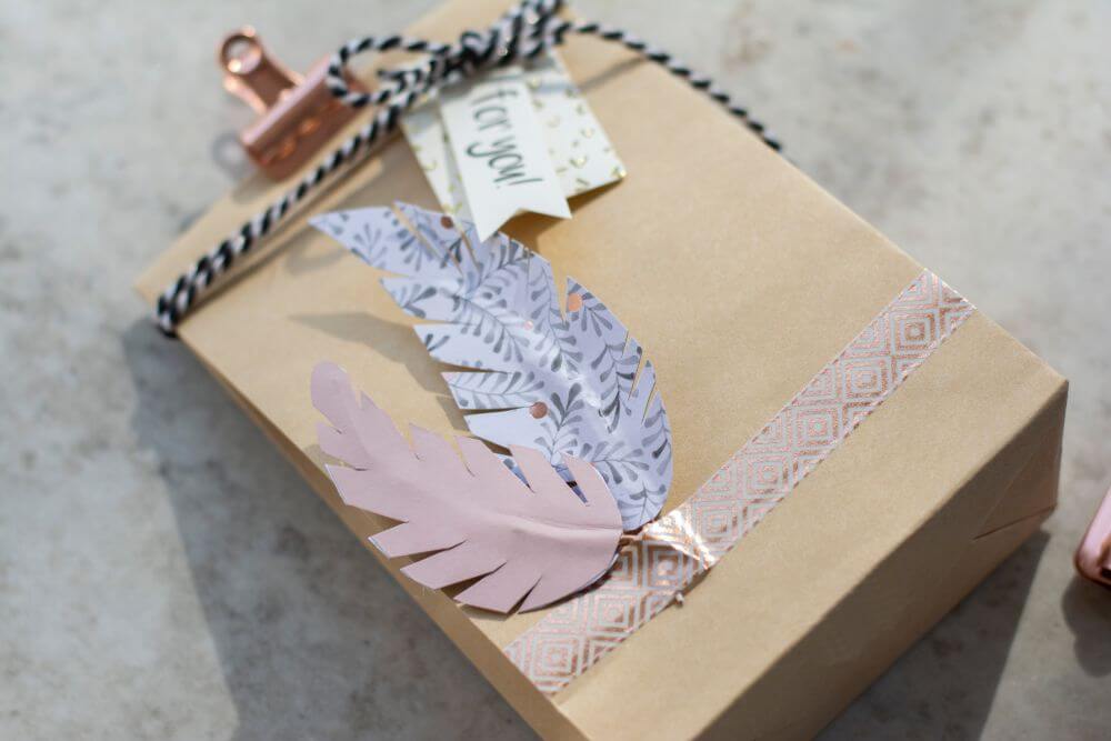 An einer Geschenktüte sind zwei Do it yourself-Papierfedern mit Maskingtape festgeklebt.