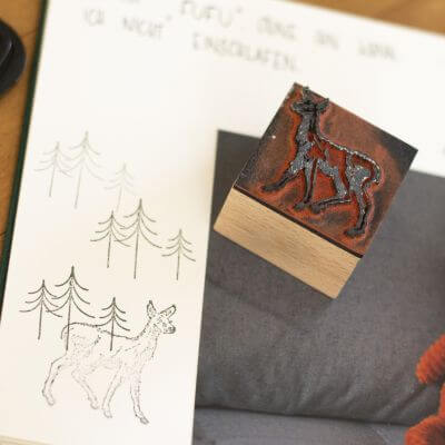 In das Fotoalbum Mini Mucho von Semikolon ist ein Foto eingeklebt, daneben sind Bäume und ein Reh gestempelt. Der Stempel mit dem Reh liegt auf dem Foto.