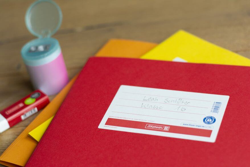 Auf einem Schreibtisch liegen verschiedenfarbige Umschläge für Schulhefte, ein Anspitzer und ein Radiergummi.