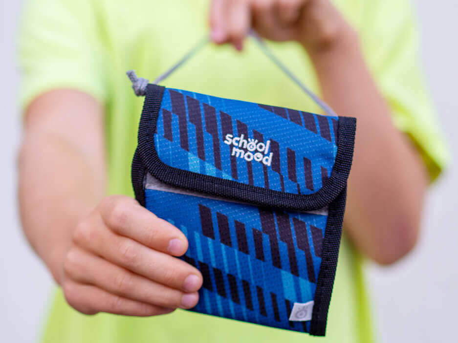 Ein Grundschulkind in einem neongelben T-Shirt hält einen blauen Brustbeutel der Firma School-Mood in die Kamera. Foto: Johanna Rundel