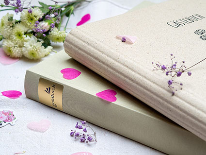 Auf einem hellen Untergrund liegen übereinander zwei hochwertige Hochzeitsgästebücher der Marke Goldbuch. Drumherum sind Papierherzen und Blumen verstreut. Foto: Johanna Rundel