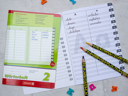 Auf einem Tisch liegen zwei Wörterhefte der Marke Brunnen. Das rechte ist aufgeschlagen und es wurden schon Wörter hineingeschrieben Außerdem liegen Buntstifte und Radiergummibuchstaben auf und um die Hefte verteilt. Foto: Johanna Rundel