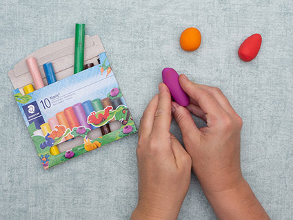 Auf einem türkisfarbenen Untergrund formt jemand Kugeln und Kegel in lila, orange und rot aus Knete von Staedtler. Foto: Johanna Rundel