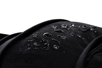 Vor einem weißen Hintergrund sieht man die Oberfläche eines schwarzen Schulrucksacks von satch. Darauf sind Wassertropfen, die vom Stoff abperlen.