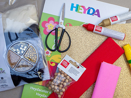 Auf einem grauen Hintergrund liegen Bastelmaterialien von Heyda und Knorr-Prandell: Tonpapier, Krepppapier, Holzperlen, Pearl Maker, Filzwolle und goldenen Perlen und Pailletten. Foto: Johanna Rundel