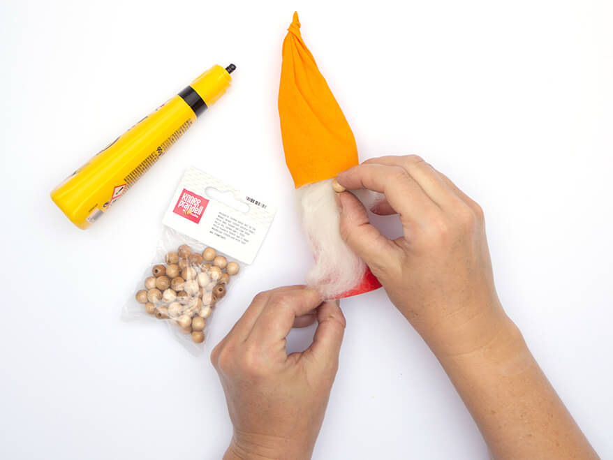 Jemand klebt eine kleine Holzperle von Knorr-Prandell als Nase auf eine als Weihnachtswichtel gestaltete Klopapierrolle. Der Untergrund ist weiß. Foto: Johanna Rundel