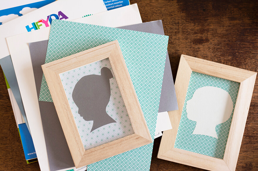 Zwei Do-it-yourself-Scherenschnitten von einem Jungen und einem Mädchen liegen in Bilderrahmen auf Papierblöcken mit unterschiedlichen Farben der Marke Heyda.