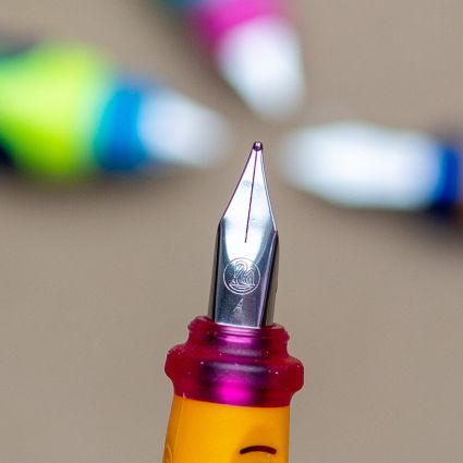 Im Vordergrund ist die Schreibfeder eines Anfängerfüllers von Pelikan zu sehen. Im Hintergrund sind weitere Füller unscharf erkennbar. Der Untergrund besteht aus Packpapier. Foto: Johanna Rundel