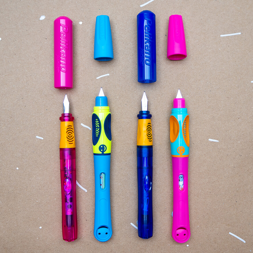 Auf einem braunen Packpapier liegen die verschiedenen Anfängerfüller der Marke Pelikan, senkrecht mit angezogener Kappe. Von links nach rechts: Ein Pelikano junior in pink/orange, ein Griffix-Schreiblernfüller in neongrün/blau, ein Pelikano junior in dunkelblau/orange und eine Griffix in pink/türkis/orange. Foto: Johanna Rundel