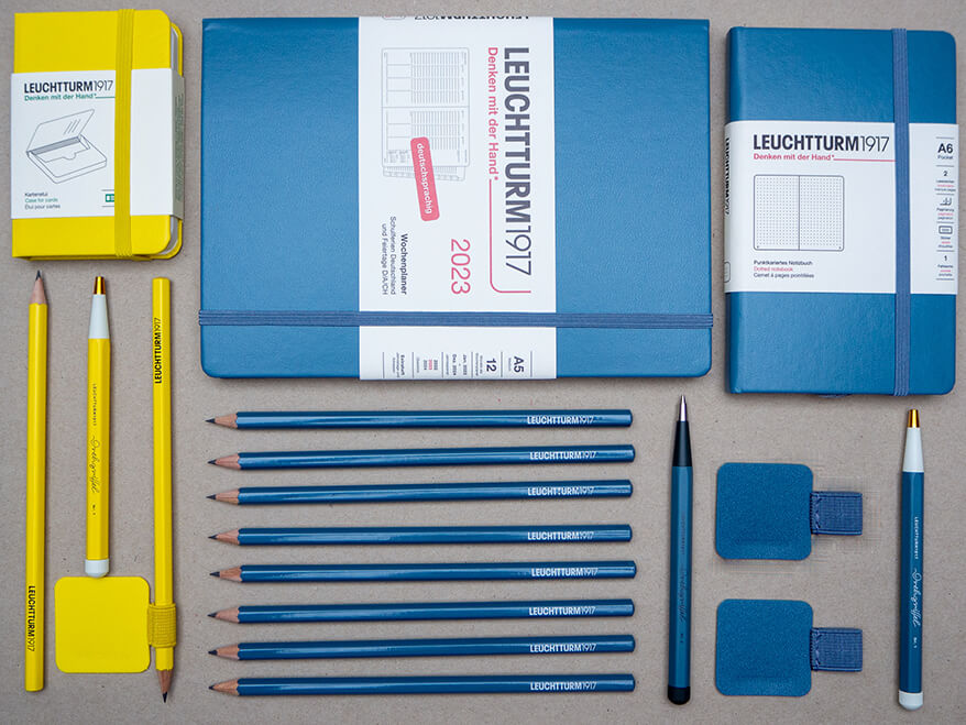 Auf einem grauen Untergrund liegen verschiedene Produkte der Marke Leuchtturm 1917. Bleistifte, Stiftschlaufen, Notizbücher und Kalender sowie Drehgriffel. Das Flatlay ist so gestaltet, dass 20% der Produkte gelb sind und links angeordnet sind. 80% sind blau und rechts daneben ausgelegt. Foto: Johanna Rundel