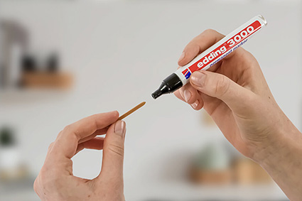 Jemand steckt eine neue Schreibspitze in einen edding 3000 Marker. Der Hintergrund ist hell und verschwommen.