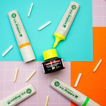 Auf einem grafischen Untergrund in Rosa, Orange und Türkis liegen vier Neon-Textmarker der EcoLine-Serie von edding. Ebenso sind eine schwarze Nachfüllkartuschen, sowie viele, über die gesamte Fläche verteilte Ersatzspitzen. Foto: Johanna Rundel