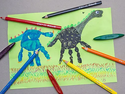 Auf einem grauen Untergrund liegt ein grünes Blatt Papier, auf dem Dinosaurier gestaltet wurden. Foto: Johanna Rundel
