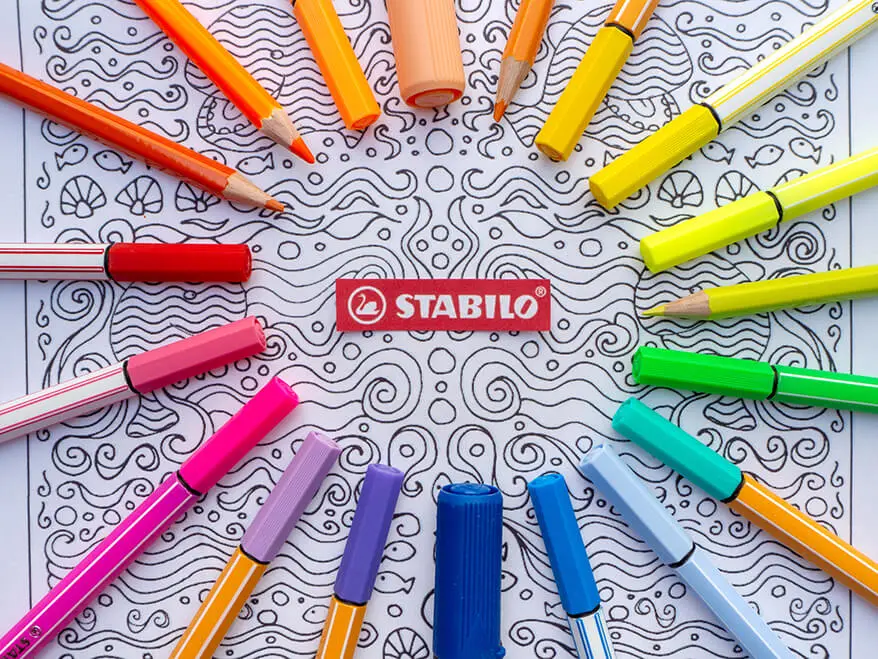 Verschiedene Bunt- und Filzstifte von Stabilo in allen Farben des Regenbogens liegen auf einer Mandala-Vorlage zum Ausdrucken.